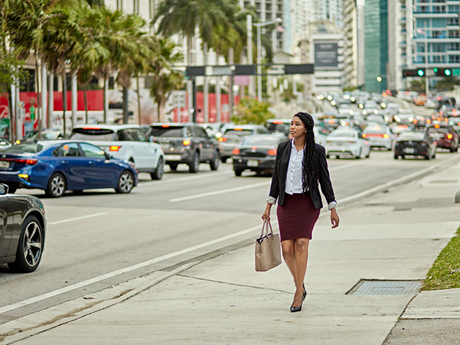 A woman walks on the sidewalk near traffic