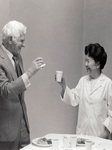 Beatrice Lei, MD and Sidney R. Garfield, MD smiling and clinking drinking glasses in celebration of her 30 years of service.
