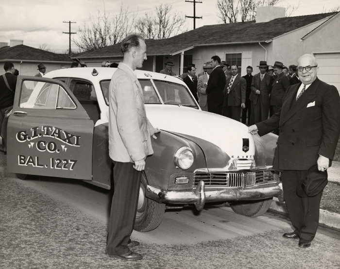 Black and white photo of Henry J. Kaiser presenting a Kaiser-Frazer car to the G.I. Taxi company