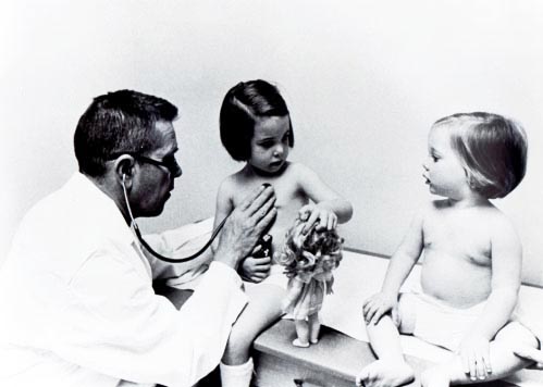 pediatrician John Smillie with two young girls inside examination room