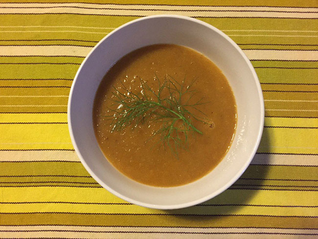 A top down view of pureed vegetable soup topped with a sprig of fresh dill.